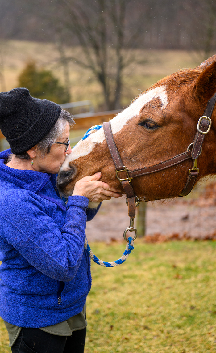Older woman gently nuzzling a horse on the nose